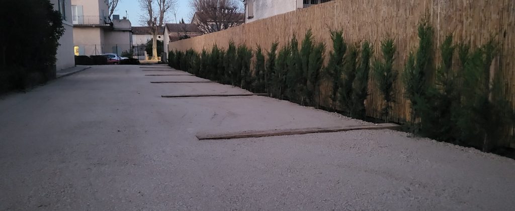 Aménagement d’un parking en gravier avec plantation d’une haie persistante le long d’une clôture en milieu urbain